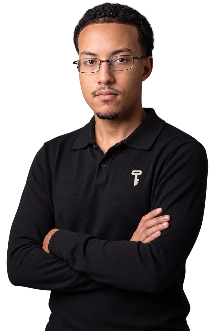 Gabriel, de óculos e camisa polo preta com o símbolo Tell Us, de braços cruzados